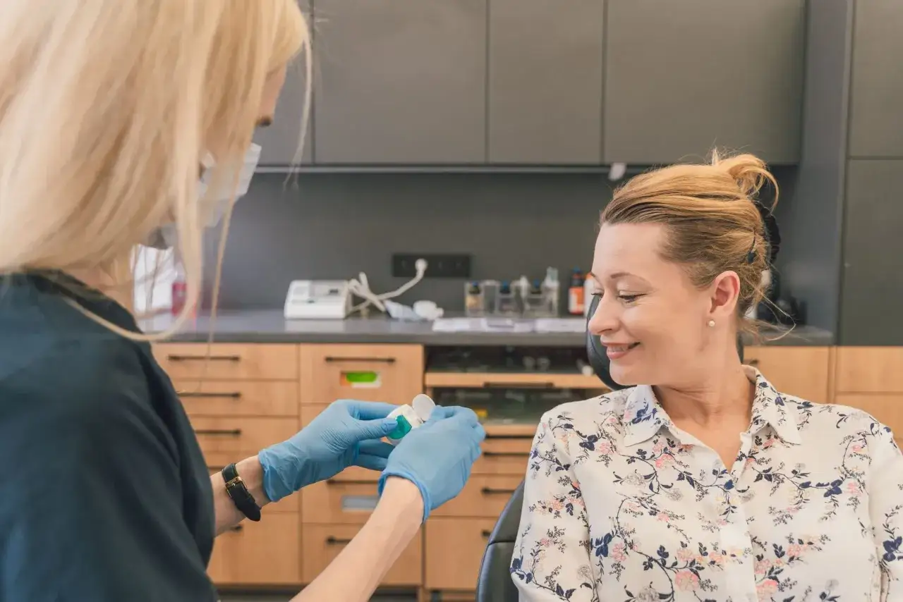 Dentystka w rękawiczkach przygotowuje preparat do fluoryzacji w ciąży. Uśmiechnięta pacjentka czeka na zabieg.