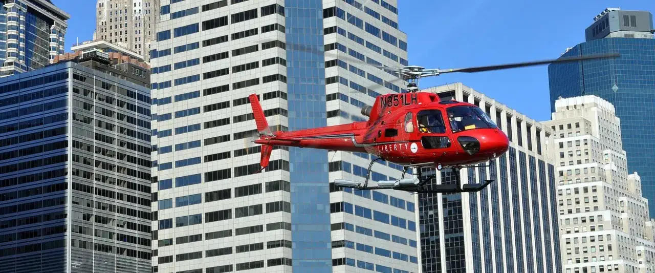 Czerwony helikopter Liberty przelatuje obok wieżowców. Zastanawiasz się, ile kosztuje lot helikopterem nad Nowym Jorkiem?