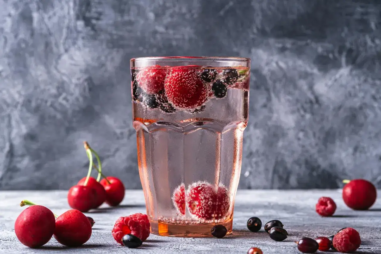 Orzeźwiający drink z wódką malinową, pełen malin, wiśni i borówek, bąbelkuje w szklance.