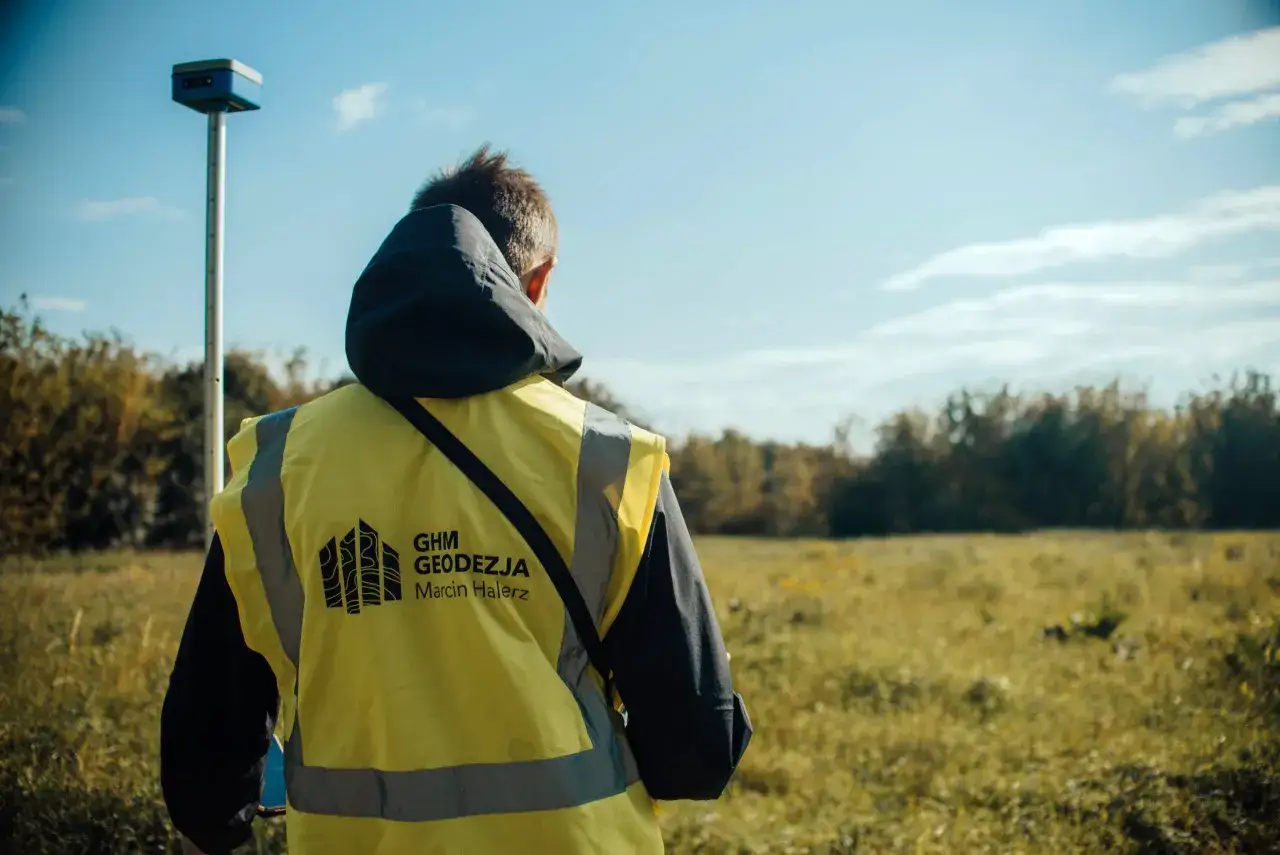 Geodeta w kamizelce odblaskowej z odbiornikiem GPS. Dowiedz się, jak znaleźć granice działki telefonem, korzystając z nowoczesnych technologii.