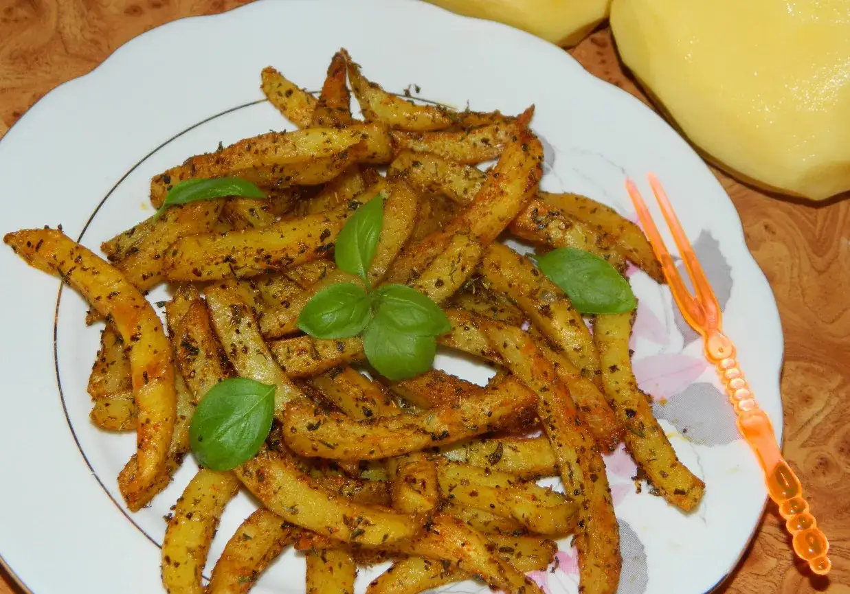 Złociste frytki z piekarnika z ziołami i bazylią na talerzu.