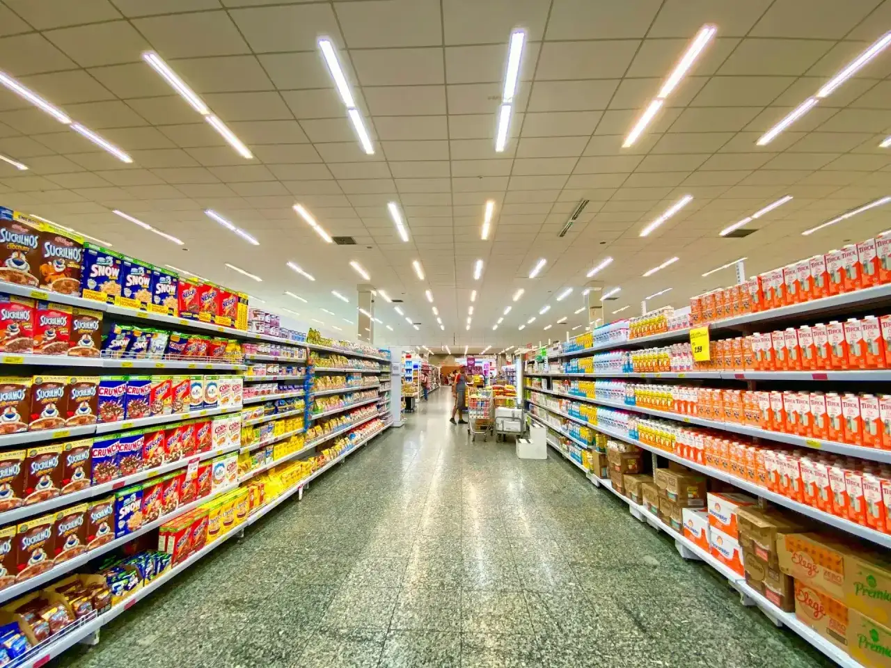 Alejka w supermarketach, pełna produktów na półkach. Widać kartony z płatkami śniadaniowymi i napojami. To typowe sklepy po angielsku, gdzie można znaleźć wszystko.
