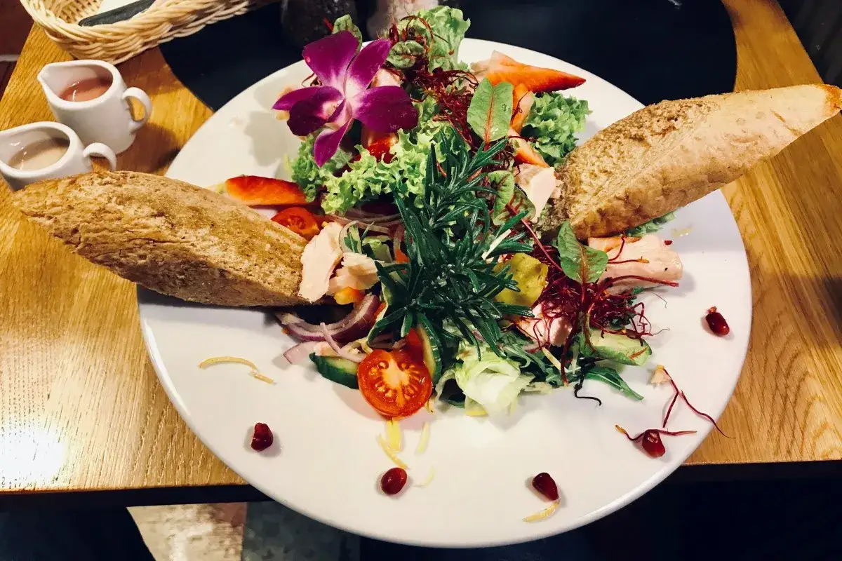 Kolorowy, świeży sałatka z rybą, pieczywem i kwiatem orchidei. Idealna propozycja, co zjesc w Jeleniej Górze.
