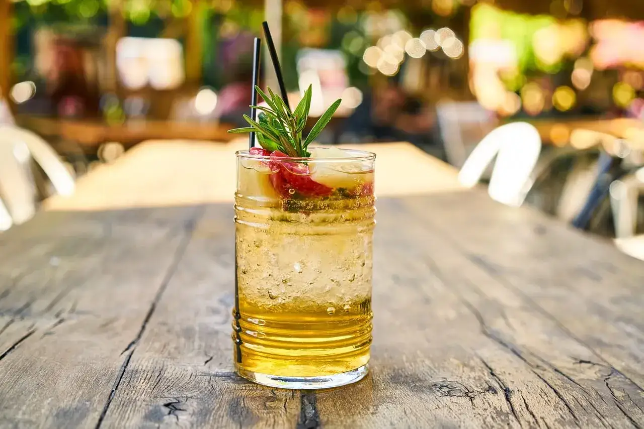Orzeźwiający drink z sokiem ananasowym, lodem i owocami, ozdobiony gałązką rozmarynu. Idealny na letnie popołudnie.