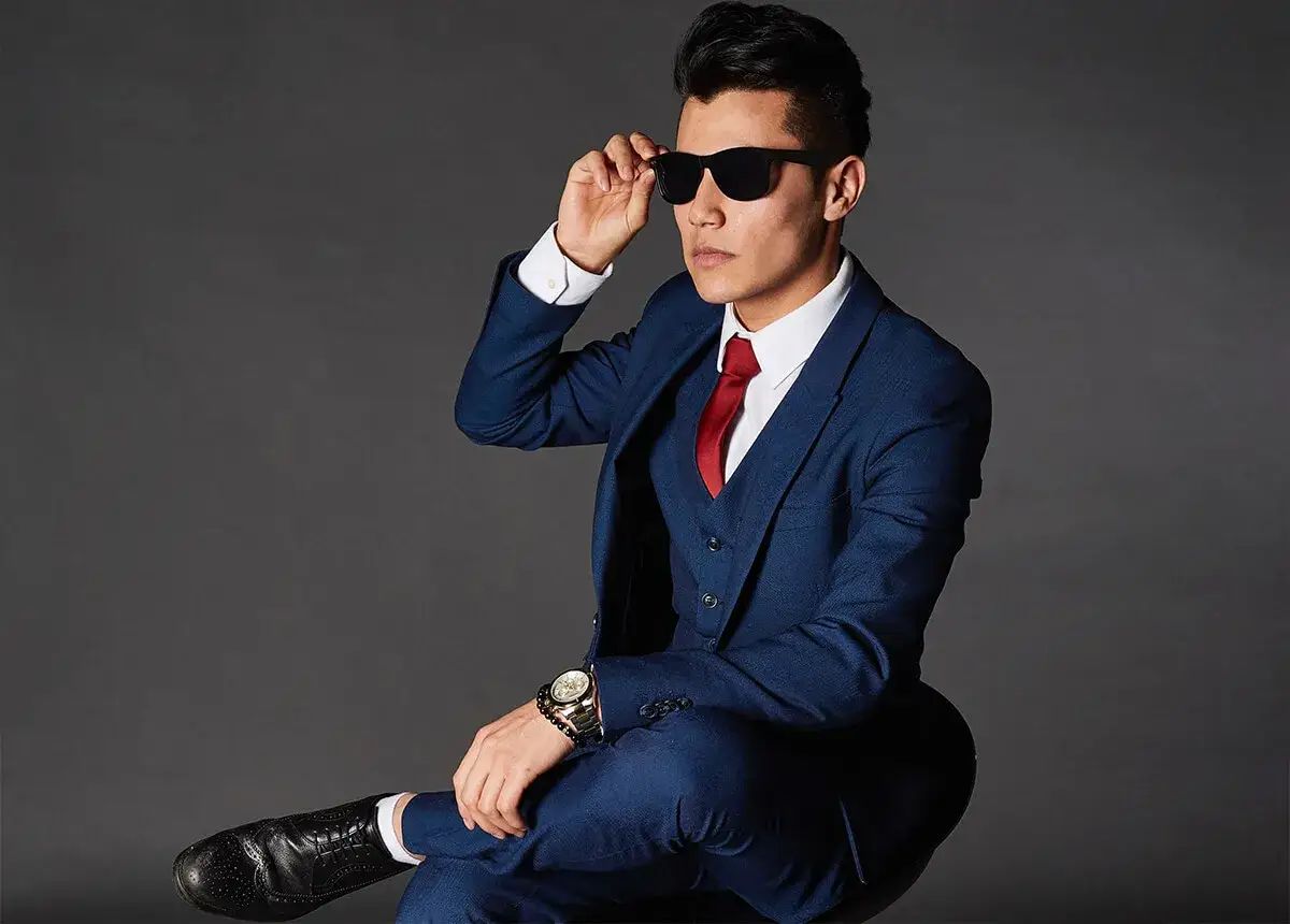Elegancki mężczyzna w granatowym garniturze i czerwonym krawacie, z okularami przeciwsłonecznymi. Idealna stylizacja: jaka marynarka do granatowych spodni.