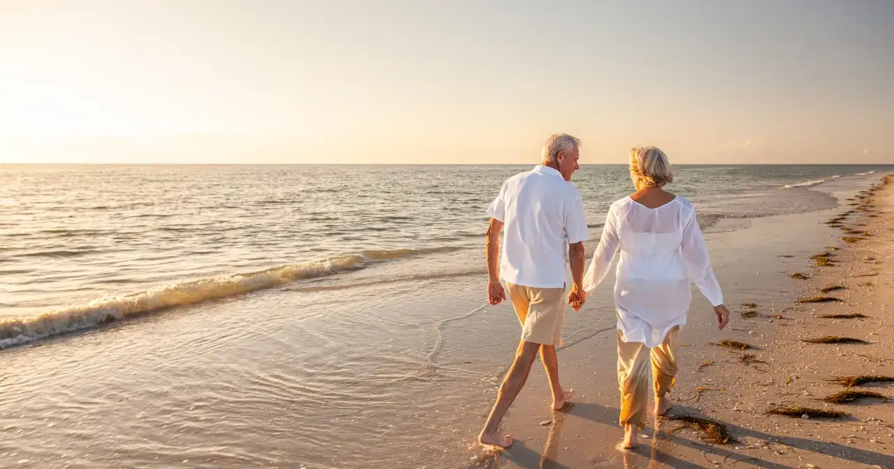 Spacerując brzegiem morza, para seniorów cieszy się zachodem słońca. Czy doczekają się bonu turystycznego dla seniorów na takie chwile?