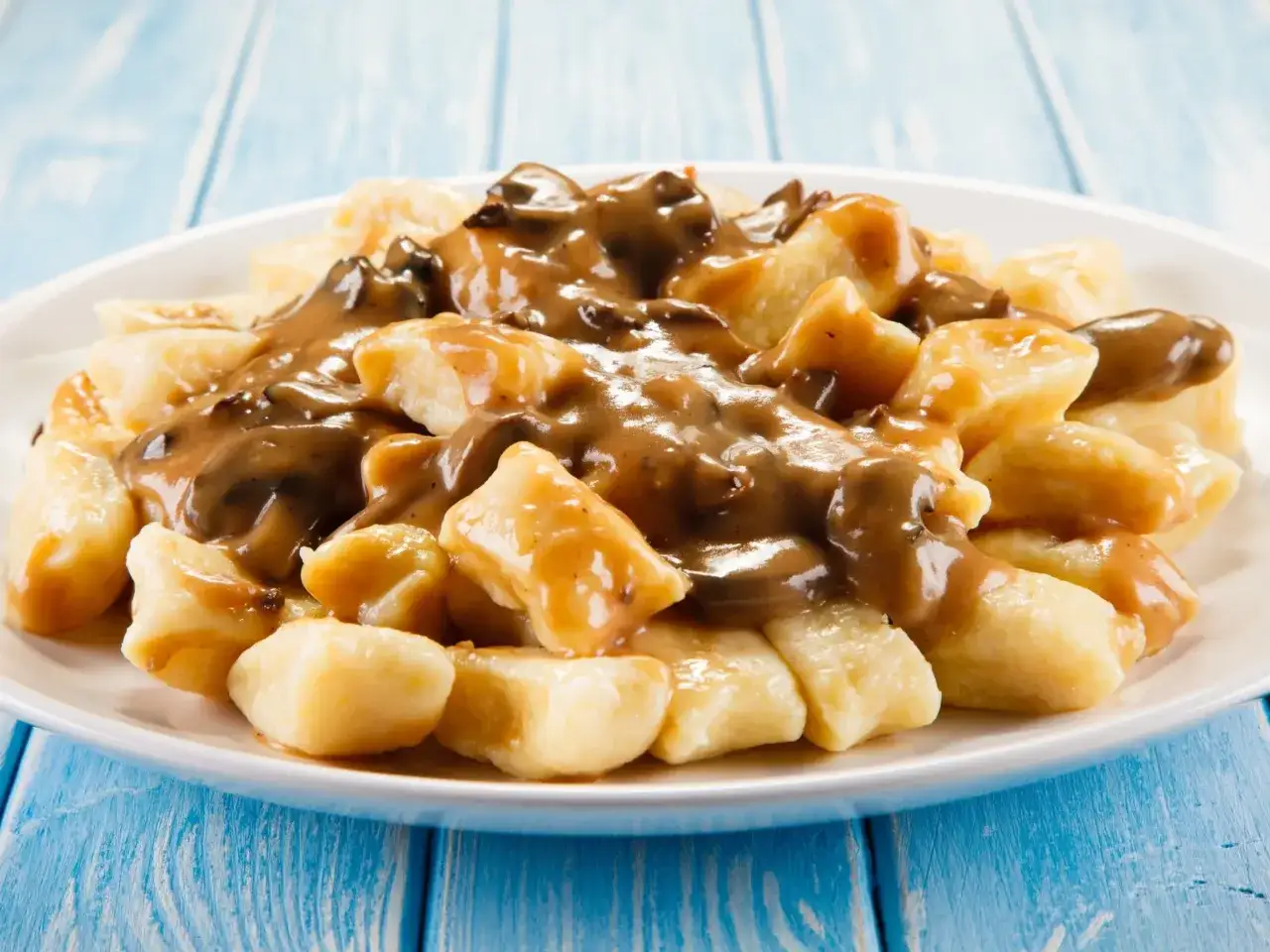 Kopytka z sosem grzybowym na talerzu, obok kopytka odsmażane na boczku. Pyszne danie obiadowe.