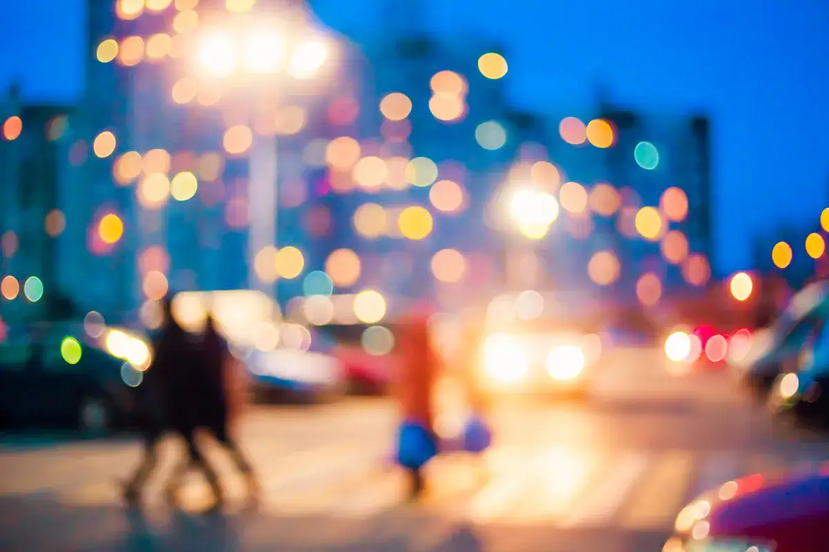 Rozmazane światła miasta i sylwetki ludzi na ulicy.