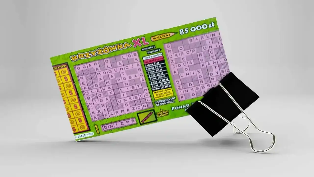 Zdrapka z krzyżówką XL z nagrodą 85 000 zł, przytrzymana przez czarny klips biurowy.