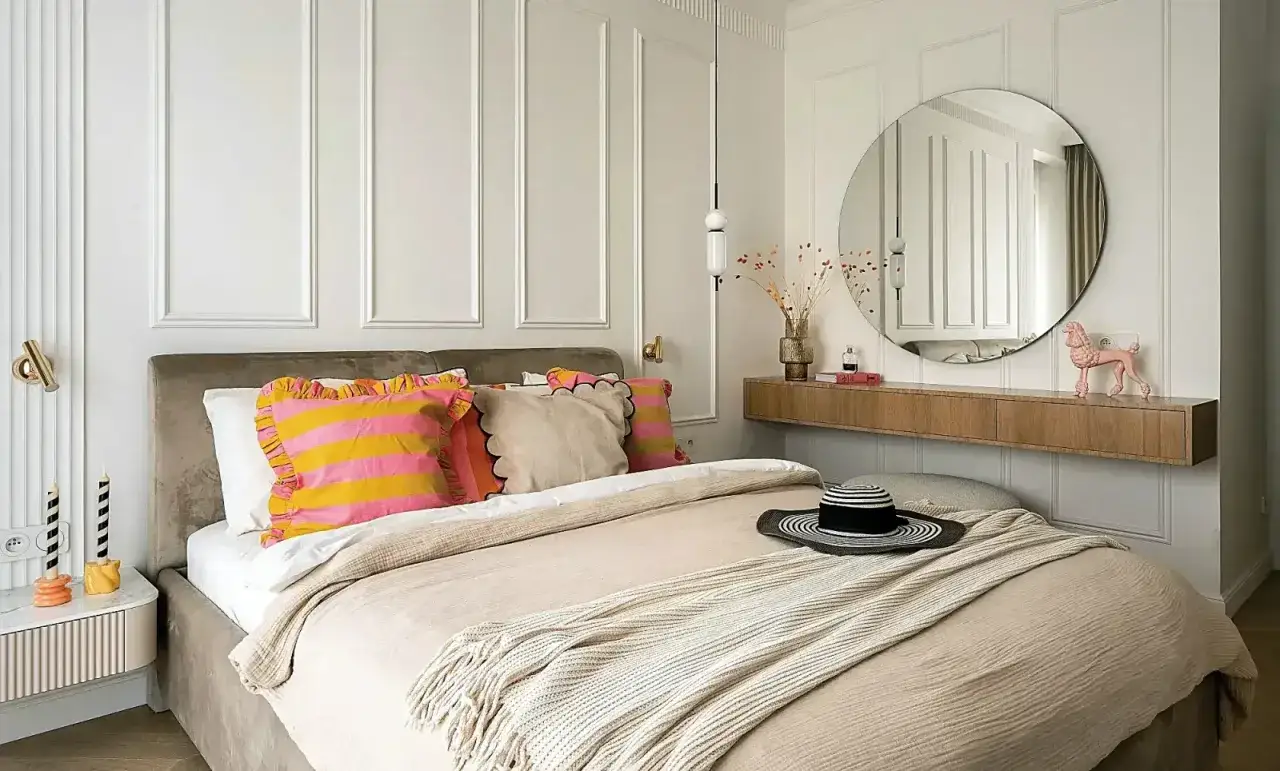 Sypialnia z łóżkiem, kolorowymi poduszkami, okrągłym lustrem i drewnianą półką.