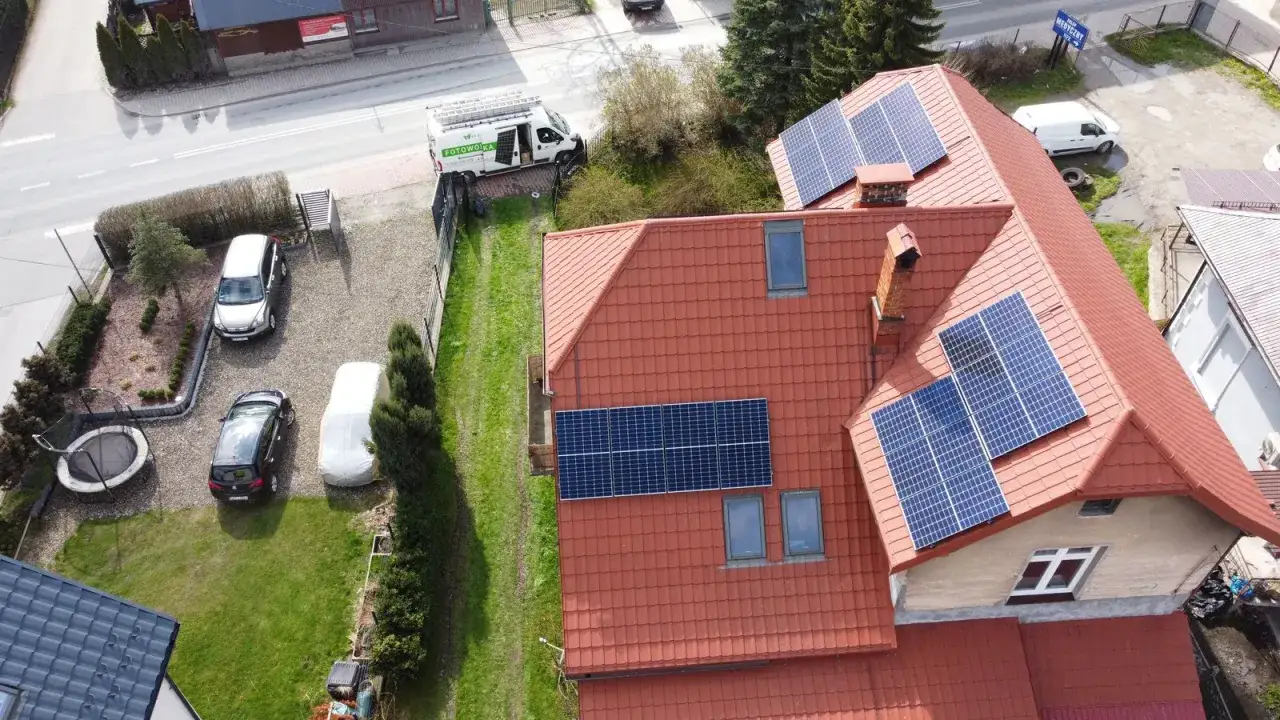 Dachówki i panele fotowoltaiczne na dachu domu. Obok stoi biały van z napisem "FOTOWOLTAIKA".