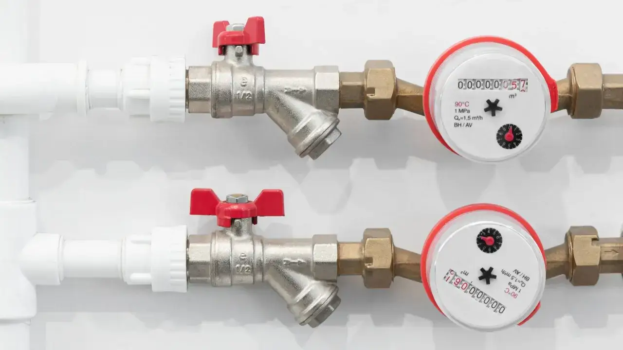 Dwa wodomierze z czerwonymi zaworami, pokazujące zużycie wody. Pomagają monitorować średnie zużycie wody na osobę.