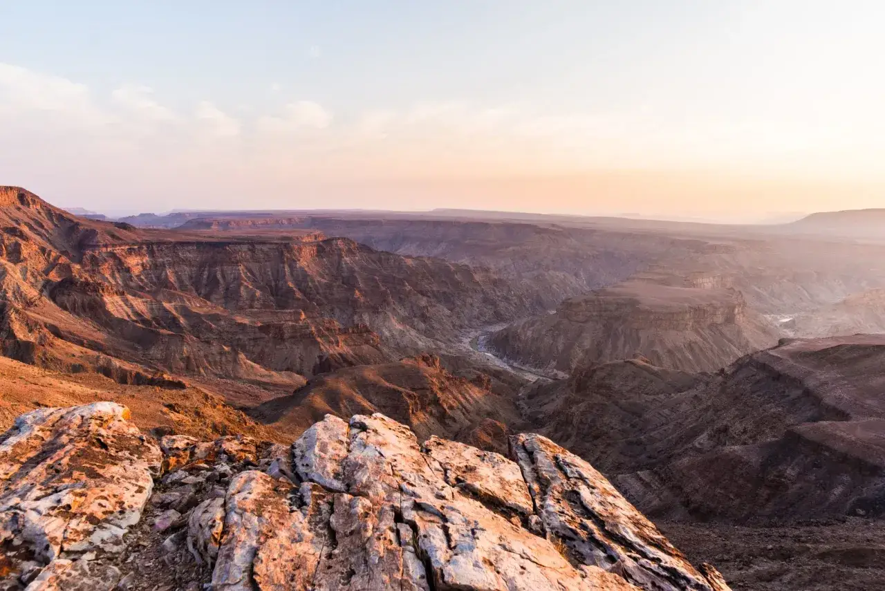 Wąwóz Fish River w Namibii, z rzeką wijącą się w dole. Zachodzące słońce maluje skały na ciepłe barwy.