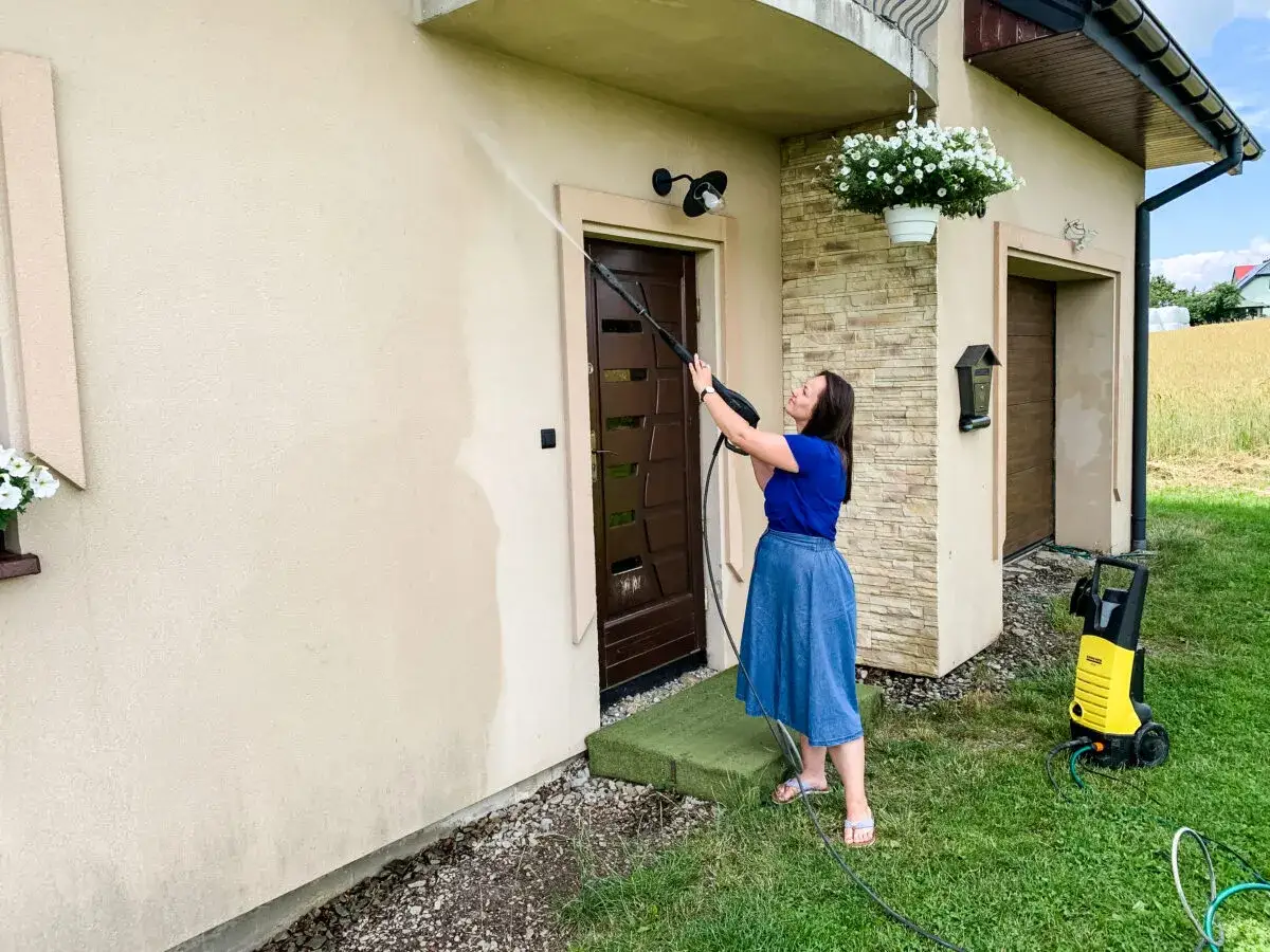 Kobieta myje elewację domu myjką ciśnieniową. Uważaj, czy myjka ciśnieniowa może zniszczyć elewację domu przy złym ciśnieniu.