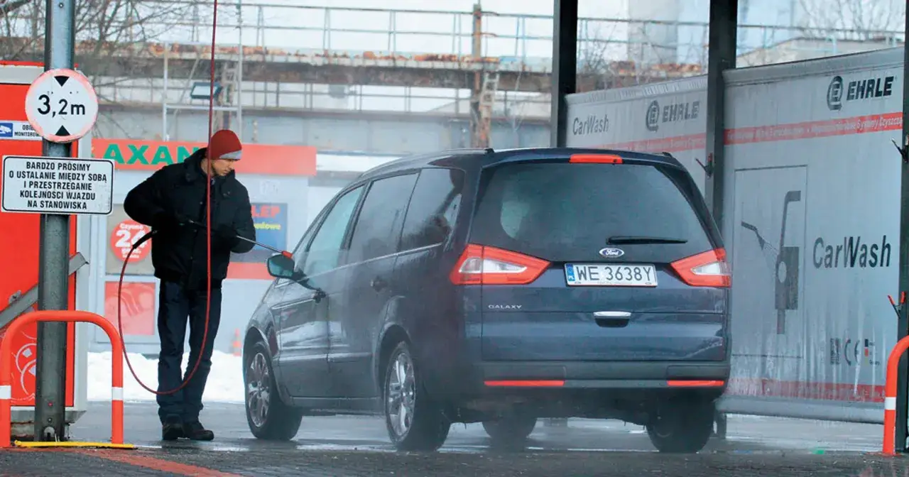 Mężczyzna myje samochód na myjni samoobsługowej. Dostępne są różne programy mycia, np. na Orlenie.