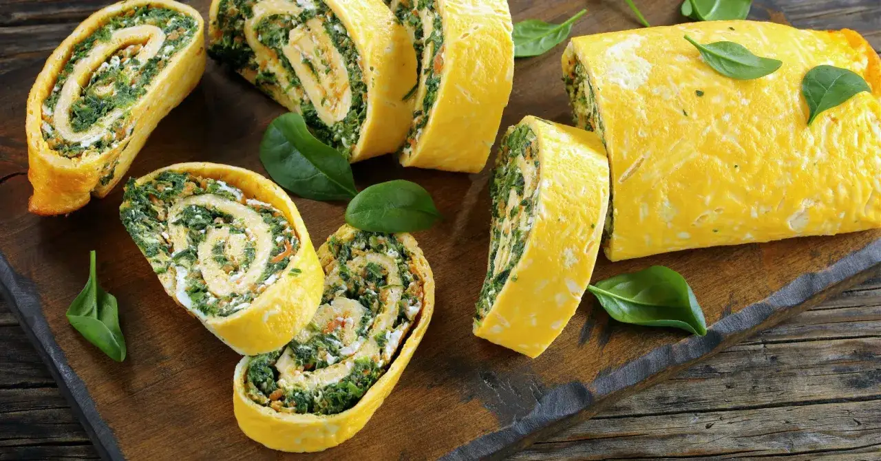 Pyszna rolada serowa ze szpinakiem, pokrojona w plastry, prezentuje się apetycznie na drewnianej desce.