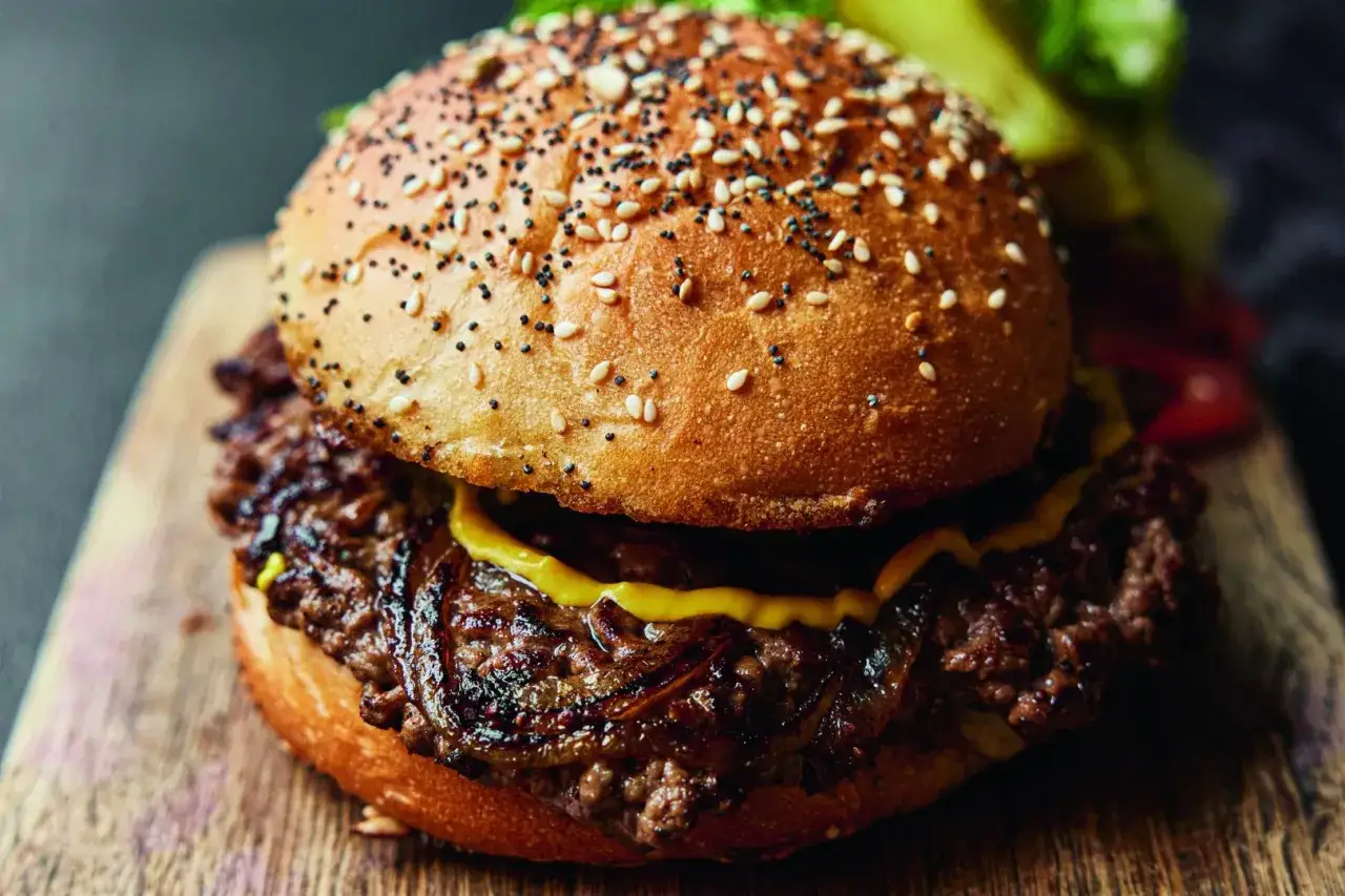 Soczysty burger wołowy z sezamową bułką i karmelizowaną cebulą na drewnianej desce.