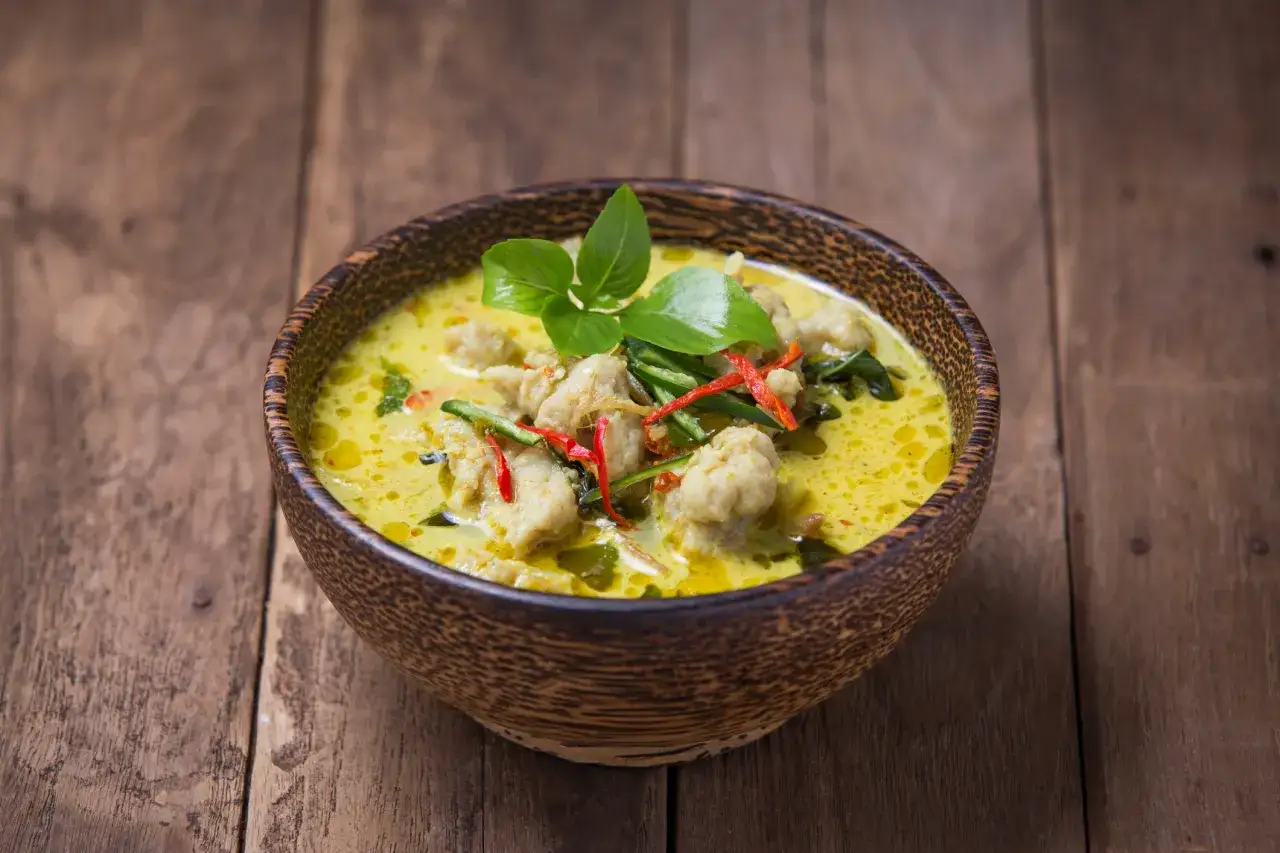 Zielone curry z kurczakiem i chili w drewnianej misce na desce.