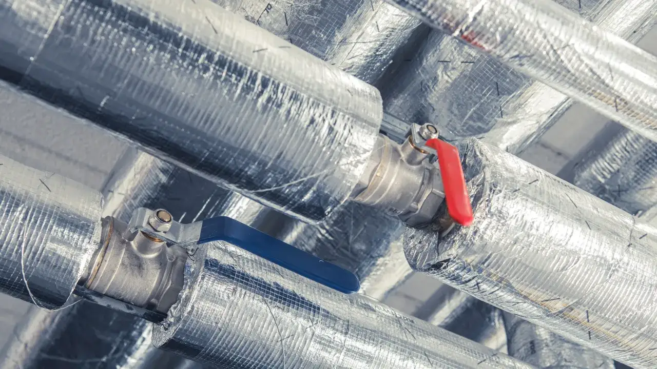 Izolowane rury CO z zaworami, jeden z niebieską, drugi z czerwoną rączką.