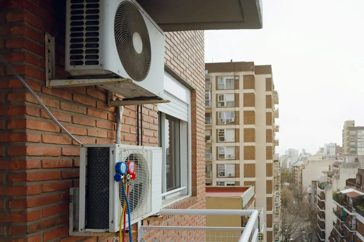 Dwa urządzenia klimatyzacyjne na ceglanej ścianie bloku, gotowe do pracy w miejskim krajobrazie.
