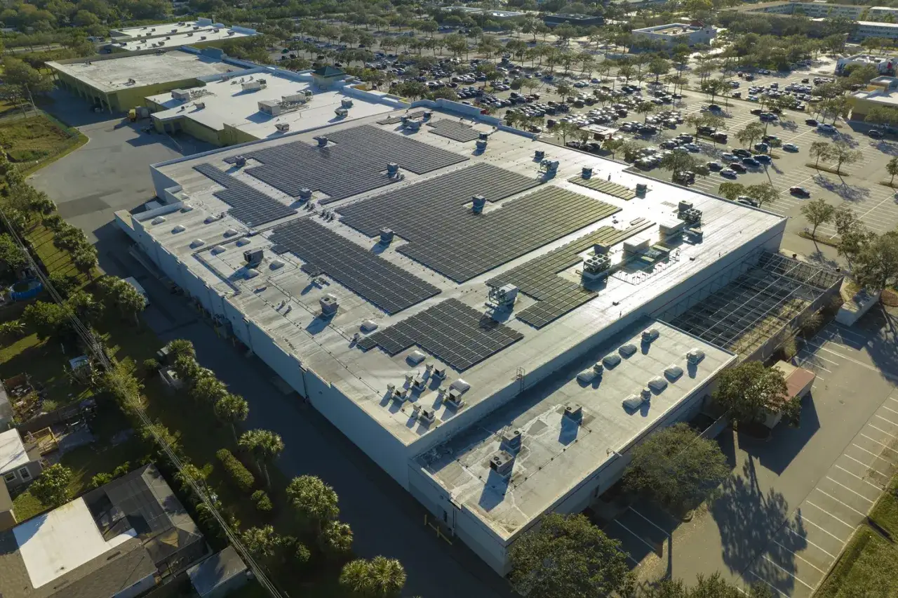 Ogromny dach pokryty panelami fotowoltaicznymi, idealny do uzyskania credit agricole kredyt na fotowoltaikę. W tle parking i drzewa.
