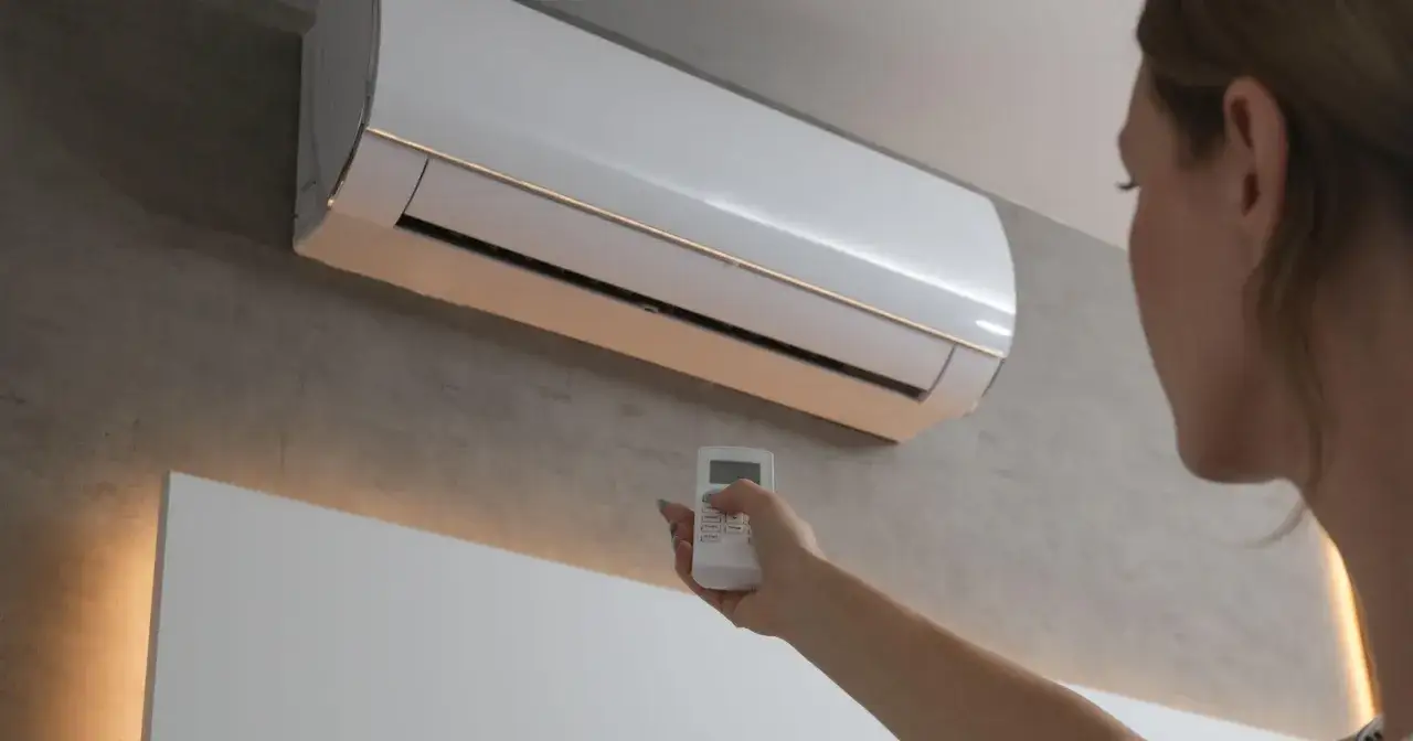 Kobieta z pilotem przy klimatyzacji. Czy klimatyzacja w domu powinna być cały czas włączona?