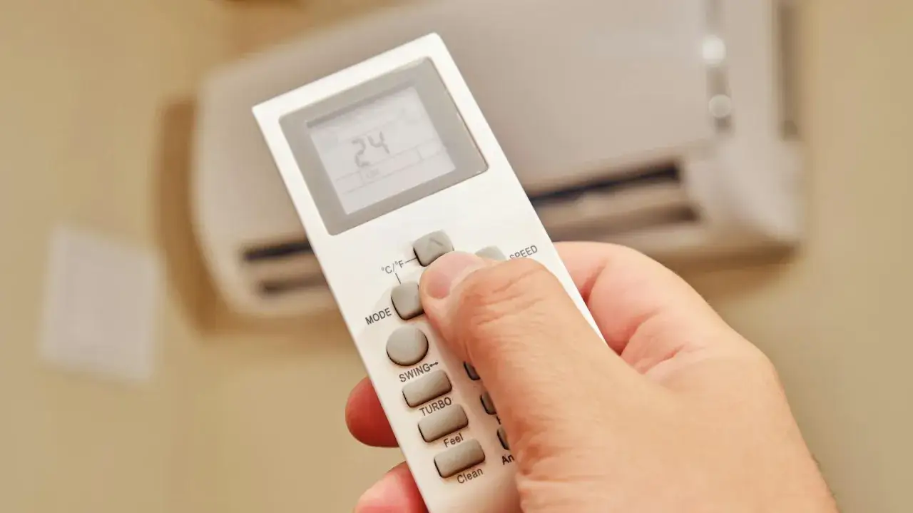 Dłoń trzyma pilot do klimatyzatora, ustawiając temperaturę na 24 stopnie. Ogrzewanie klimatyzatorem zapewnia komfort.
