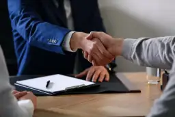 Dwaj mężczyźni ściskają sobie dłonie nad dokumentami, finalizując umowę o dzieło.