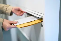 Main tenant insère des enveloppes dans une boîte aux lettres. Le délai recommandé pour la réception est important.