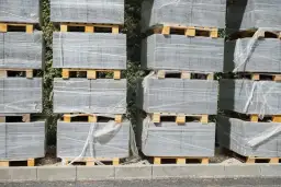 Stosy palet z szarą kostką brukową owiniętą folią.