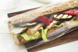 Pan kanapka z kurczakiem, grillowanymi warzywami i sałatą, zapakowana w folię. Idealna na szybki lunch w Warszawie.