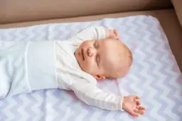Uśmiechnięte dziecko śpi na kolorowej pościeli. To idealny moment, kiedy dziecko powinno spać bez pieluchy, czując się swobodnie i komfortowo.