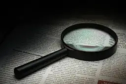 Lupa powiększa tekst, symbolizując dociekliwość i spostrzegawczość – kluczowe cechy dobrego detektywa.