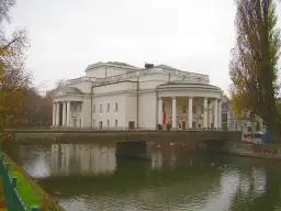 Teatr Kalisz zaprasza na spektakle. Imponujący budynek z kolumnadą nad rzeką, jesienne drzewa.