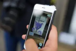 Ręka trzyma smartfon, na ekranie którego widnieje fioletowy Haunter, jeden z typów pokemonów.