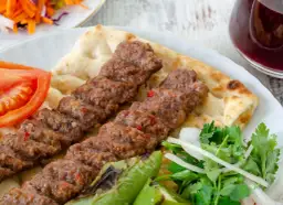 Pyszny Adana kebab przepis na talerzu z pitą, pomidorem, papryką i sałatką. Idealny na letni obiad.
