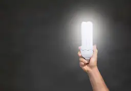 Dłoń trzymająca energooszczędną żarówkę, która emituje jasne światło. Zastanawiasz się, ile lumenów na m2 zapewni?