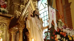 Figura Jezusa z chorągwią z krzyżem, otoczona złotymi zdobieniami i kwiatami. Symbolizuje zwycięstwo i nadzieję, przypominając o tym, ile trwaja rezurekcje.