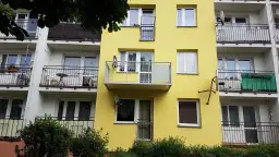 Żółty blok z balkonami. Widać, jak przedłużyć balkon betonowy, dodając nowoczesną, metalową konstrukcję.