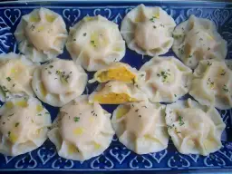 Pyszne pierogi z dynią, polane masłem i posypane szczypiorkiem, ułożone na niebieskiej paterze.