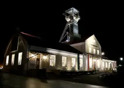 Wieczorem przy szybie kopalni Wieliczka, gdzie można kupić bilety, widać oświetlone budynki i wieżę wyciągową.