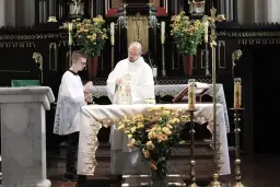 Ksiądz i ministrant podczas mszy świętej przy ołtarzu ozdobionym kwiatami.