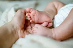 Dłoń dorosłego obejmuje stópkę niemowlaka na miękkim tle.