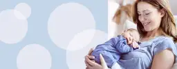 Uśmiechnięta mama tuli śpiącego noworodka w szpitalu. Podpowiadamy, jak ubrać noworodka w szpitalu, by czuł się komfortowo.