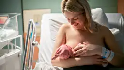 Uśmiechnięta mama karmi piersią noworodka. Pierwsze krople siary z piersi to cenny początek dla maluszka.