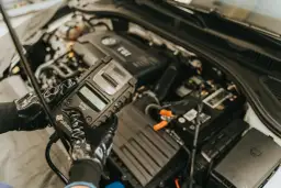 Mechanik w rękawiczkach sprawdza stan akumulatora za pomocą testera, który może również diagnozować czujnik halla w samochodzie.
