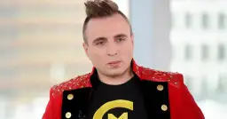 Czadomen w czerwonej marynarce z ćwiekami i czarnej koszulce z żółtym logo.