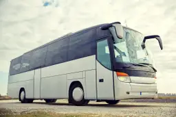 Biały autokar turystyczny na tle nieba z chmurami.