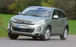 Zielony Citroën C4 Aircross z polskimi tablicami WE 674GE jedzie po drodze wśród zieleni.
