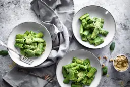 Drei Teller mit Rigatoni in cremiger, grüner veganer Spinatsoße, bestreut mit veganem Parmesan. Ein Genuss für Augen und Gaumen!